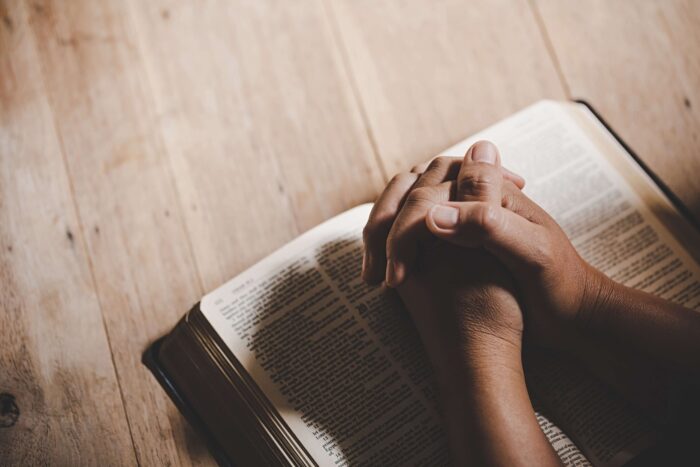 Two hands in prayer over a bible. Religion is one of the main differences between mexico and the USA.