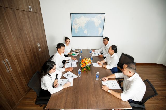 Vietnamese colleagues discussing reports around a conference table during a formal business meeting.