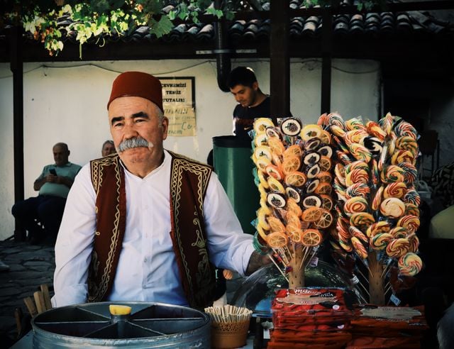 Traditional Turkish sweet seller welcoming customers at a market stall.