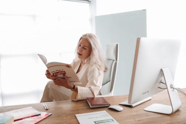 Professional woman studying English independently with a textbook at her desk.