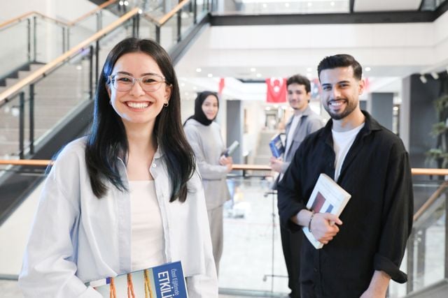 Students holding books in a university setting with Turkish flags in the background, representing learners studying Turkish pronunciation and grammar.