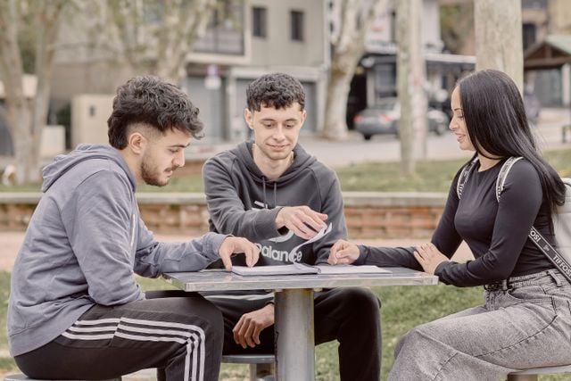 Three students studying together at an outdoor table, illustrating collaborative learning and strategies for understanding long German sentences.