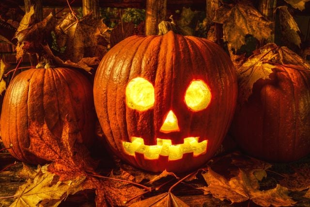Glowing jack-o'-lantern with a carved face surrounded by pumpkins and autumn leaves